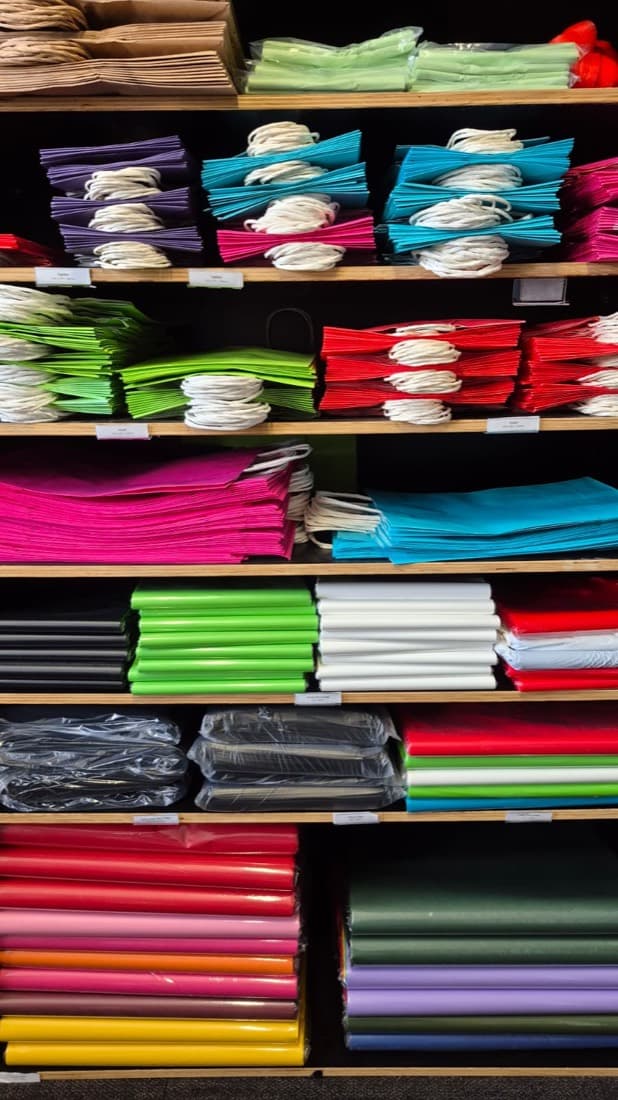 Shelves stocked with brightly coloured craft materials, tissue paper, foam sheets and rolled card in many colours