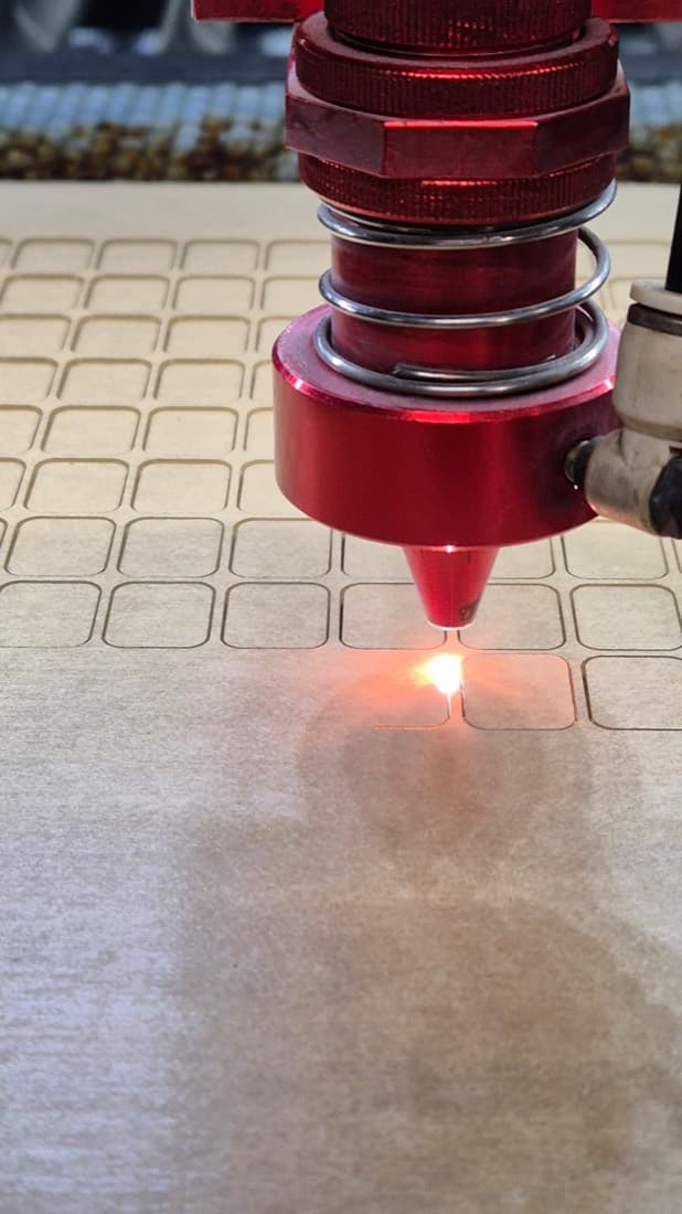 Close-up of a laser engraving head etching small rounded tags into a wooden craft panel
