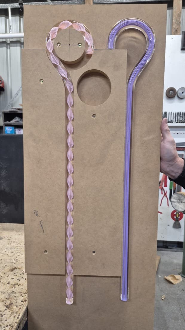Custom pink and purple twisted acrylic art components laid out on an MDF jig in the workshop