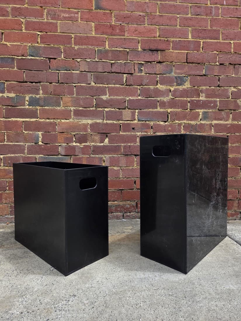 Two black plastic storage boxes with cut-out carry handles fabricated for site use