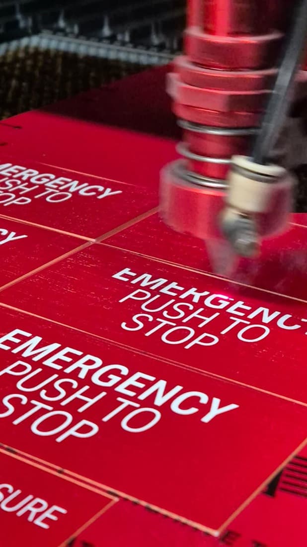Laser machine engraving red and white EMERGENCY PUSH TO STOP traffolyte switchboard labels
