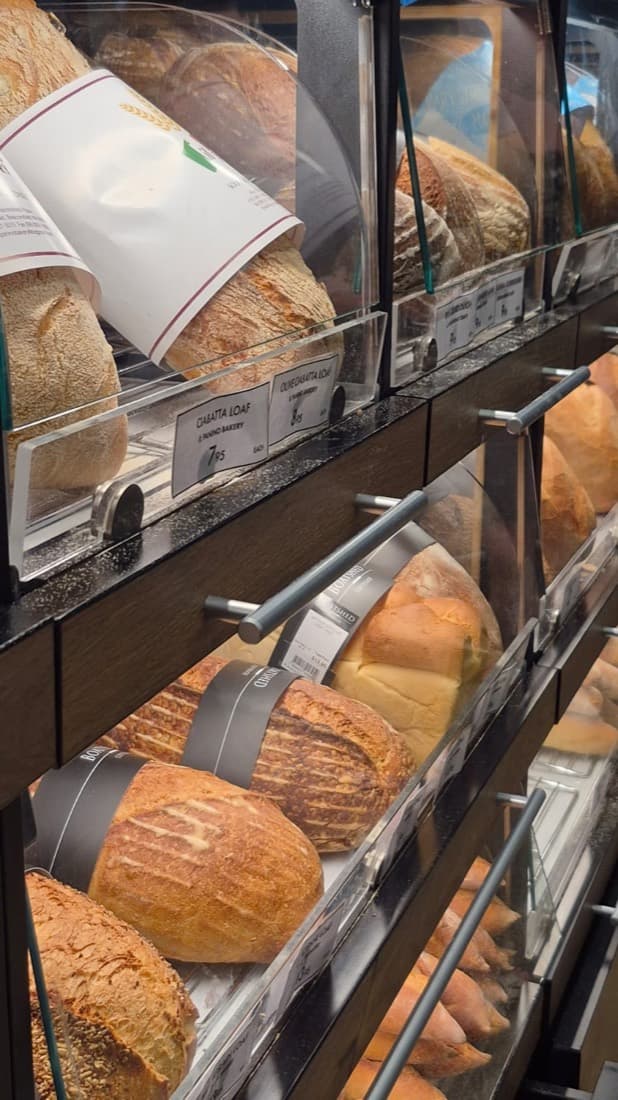 Cafe bakery display shelves of fresh bread loaves behind clear acrylic sneeze guards and food covers