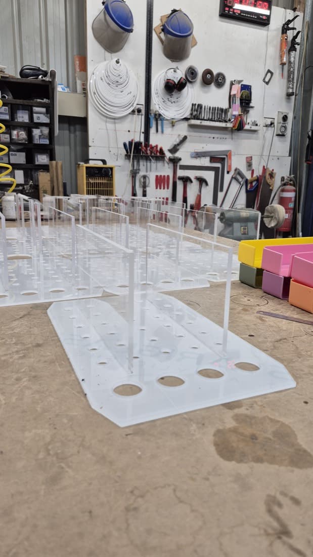 Batch of clear acrylic test-tube racks fabricated and laid out on the workshop floor