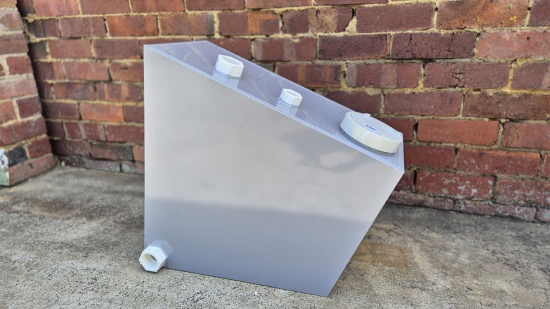 Custom fabricated angled plastic tank with threaded fittings against a brick wall