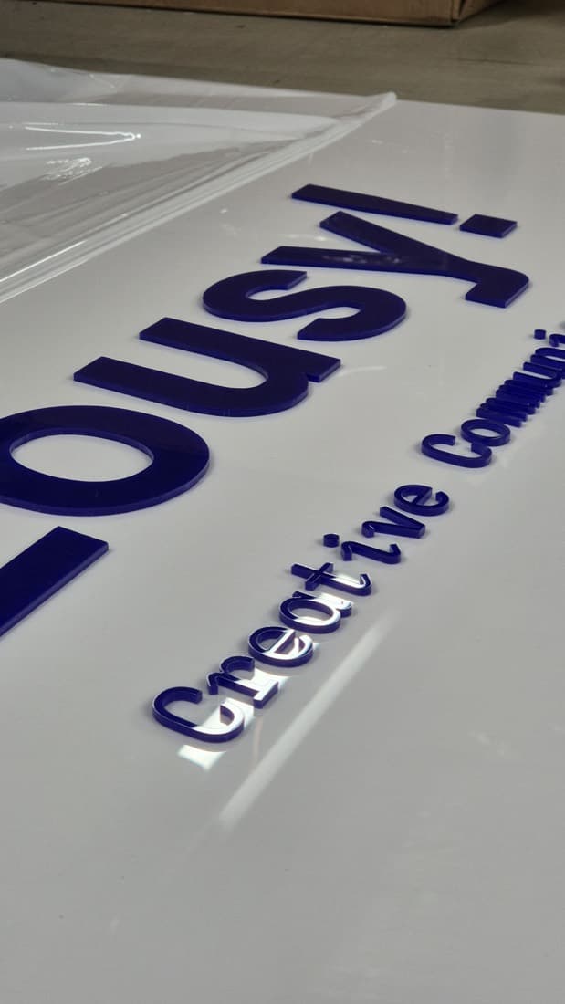 Raised purple acrylic lettering spelling a creative community brand name on a white sign panel