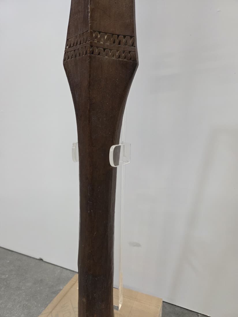 Carved wooden artefact held upright on a custom clear acrylic display stand