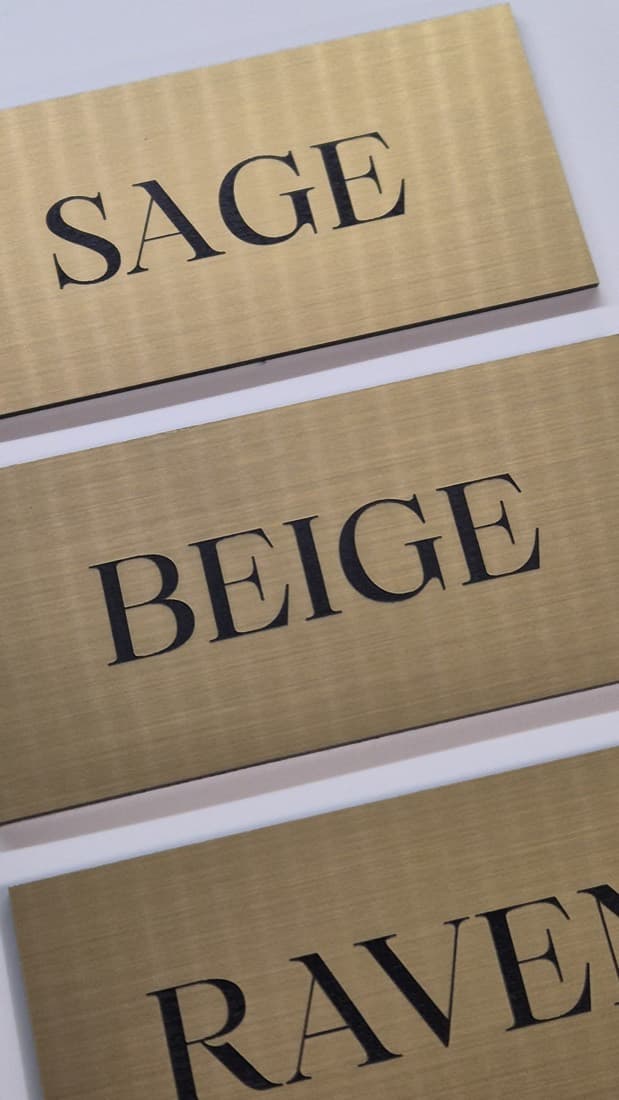Engraved brushed-brass-look acrylic name plates reading Sage, Beige and Raven