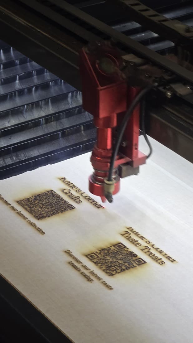 Laser cutter engraving QR-code visitor signage onto a plywood sheet